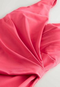 Tissu rose drapé en plis, présentant une texture lisse et un détail de design torsadé au centre.