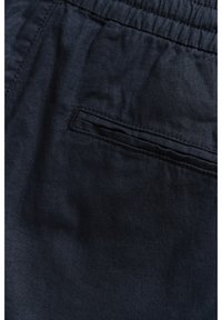 Gros plan sur un pantalon avec une ceinture élastique bleu marine foncé et une poche passepoilée horizontale unique cousue sur le tissu.
