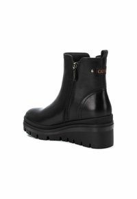 Botines de cuero negro con una suela gruesa, cremallera lateral y una lengüeta en la parte posterior. Presentan un parche con el logo cerca de la cremallera.