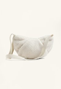 Bílá umělá vlna crossbody taška s kulatým tvarem, měkkou texturou a plochým béžovým popruhem pro snadné nošení.