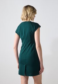 Rochie verde smarald cu mâneci scurte, croi slim, fermoar la spate și slit posterior pentru mobilitate. Fabricată dintr-un material neted și elastic.