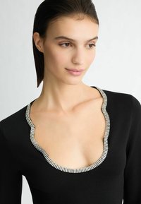 Top nero con scollatura profonda a scalloped, accentuata da un bordo metallico scintillante. Il tessuto appare liscio e aderente.