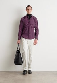 Donkerpurperen overhemden in slim fit, gecombineerd met witte broeken. Het model houdt een zwarte totebag vast, draagt zwarte schoenen en een coltrui.