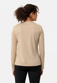 Beige langermet topp med rund hals, glatt tekstur, subtilt mønster og en grønn etikettakent nær kanten, sammen med svarte leggings.