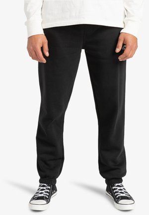 Black sweatpants with elastic cuffs, made of soft fabric. Worn with a white long-sleeve shirt and black sneakers featuring white accents.