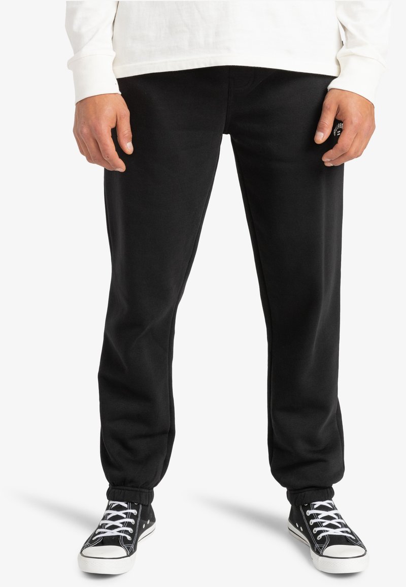 Black sweatpants with elastic cuffs, made of soft fabric. Worn with a white long-sleeve shirt and black sneakers featuring white accents.
