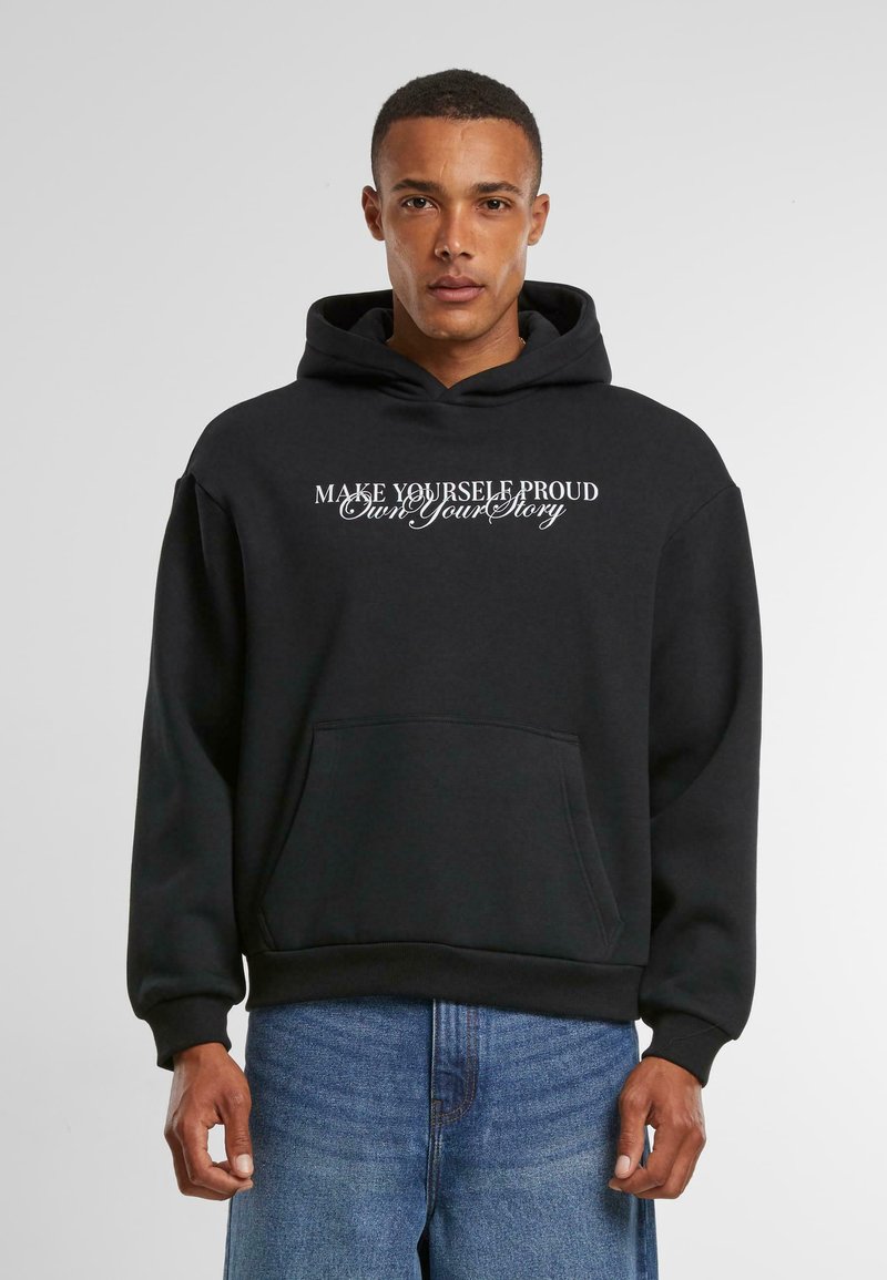 Sort hætte sweatshirt med forlommer og hvid tekst, der siger "GØR DIG SELV STOLTHED - Ejer din historie." Glat stof med ribbede mansjetter.