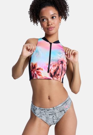 Kobieta w bezrękawnikowym krótkim topie z tropikalnym wzorem zachodu słońca i z przodu zamkiem oraz czarno-białych, wzorzystych majtkach bikini.