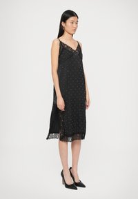 Fekete szatén ruha csipke díszítéssel, pöttyös mintával, állítható pántokkal és csipke szegéllyel az alján. Hossza a térd alatt ér véget.