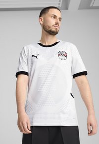 Biela futbalová dres s čiernymi akcentmi, zdobený geometrickými vzormi, logom Puma a emblemom národného tímu Egypta na hrudi.