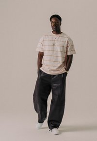 T-shirt a righe rosa chiaro con maniche corte, abbinata a pantaloni baggy neri in pelle. Il modello indossa sneakers bianche e collane sovrapposte.