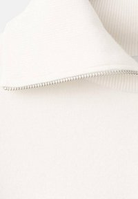 Bela pulover z zadrgo in visokim ovratnikom, s teksturo rebrastega vzorca ter srebrnim dodatkom zadrge vzdolž izreza ovratnika.