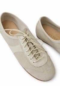 Scarpe in suede beige con dettagli in pelle, punta tonda e design con lacci. Presentano una finitura testurizzata e una suola in gomma. Stile minimalista.