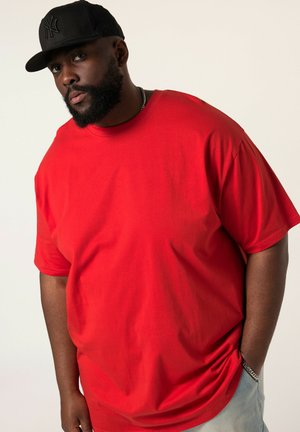 Red cotton t-shirt with a relaxed fit and short sleeves. Notable smooth texture. Worn with a black baseball cap, silver chain visible.