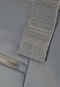 Borsa in tessuto grigia con una robusta tracolla caratterizzata da cuciture testurizzate e un dettaglio zip a contrasto, realizzata in un tessuto liscio e durevole.