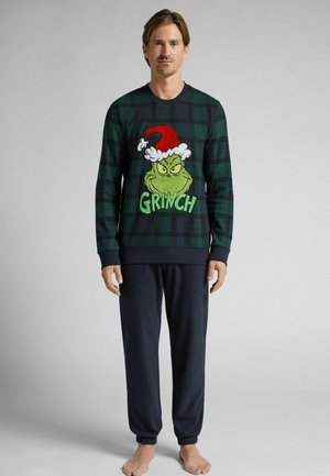 Blusa de manga larga a cuadros verdes y negros con un gráfico bordado del Grinch que lleva un gorro de Santa rojo, combinada con pantalones de puños elásticos en azul marino.
