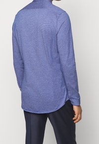 Lange mouwen shirt in lichtblauw, gestructureerde stof. Heeft een gebogen zoom, met knopen, en een contrasterende kraag. Eenvoudig, modern ontwerp.