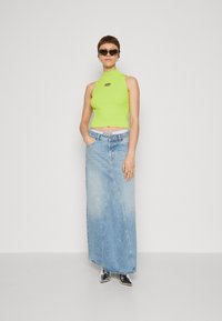 Neon green sleeveless top with a high neckline, paired with a light blue denim maxi skirt featuring a curved hem and pockets.