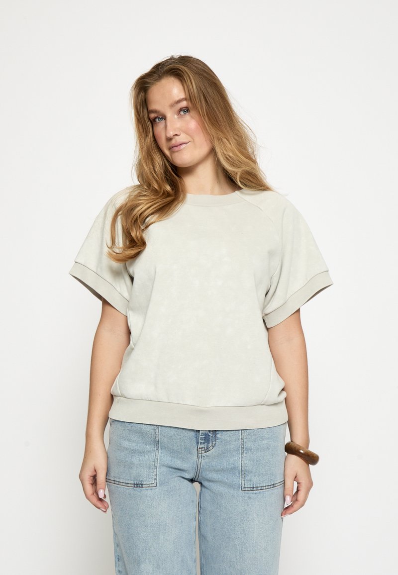 Hellgrauer Pullover mit weicher Textur, kurzen Raglanärmeln, gerippten Bündchen und rundem Ausschnitt, kombiniert mit lockeren Jeans.