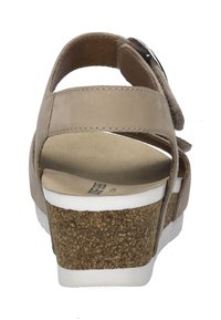 Beige leren sandaal met verstelbare band, kurken wedge hak en witte rubberen zool. Achteraanzicht toont een gladde textuur en minimale details.