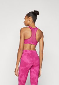 Sujeción rosa ajustado con diseño de espalda nadadora, hecho de material suave. Combinado con leggings rosa de tiro alto que presentan un patrón sutil.