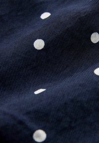 Tissu bleu marine avec une texture côtelée, présentant un motif de pois blancs uniformément espacés.