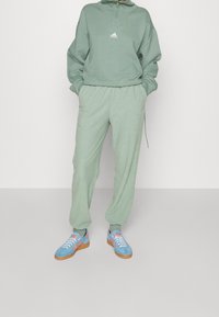 Ljusgrön hoodie med halv dragkedja och logotyp, matchad med gröna joggers. Skorna har blått med rosa och orange accenter.