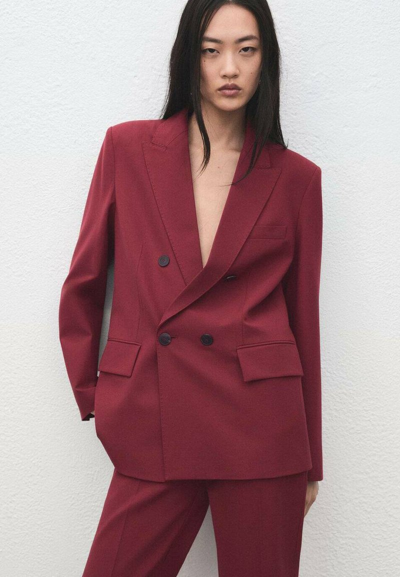Bordowa marynarka dwurzędowa z klapami z wycięciem, dwoma przednimi kieszeniami i czarnymi guzikami; w komplecie z dopasowanymi spodniami. Gładka faktura.
