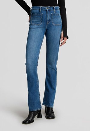 Jean bleu droit avec poches plaquées à l'avant, porté avec des bottines noires à talons et un haut noir côtelé.