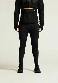 Schwarze Sportleggings kombiniert mit einem strukturierten schwarzen Langarmoberteil mit Reißverschluss und orangefarbenen Akzenten. Zusätzlich schwarze Schuhe.