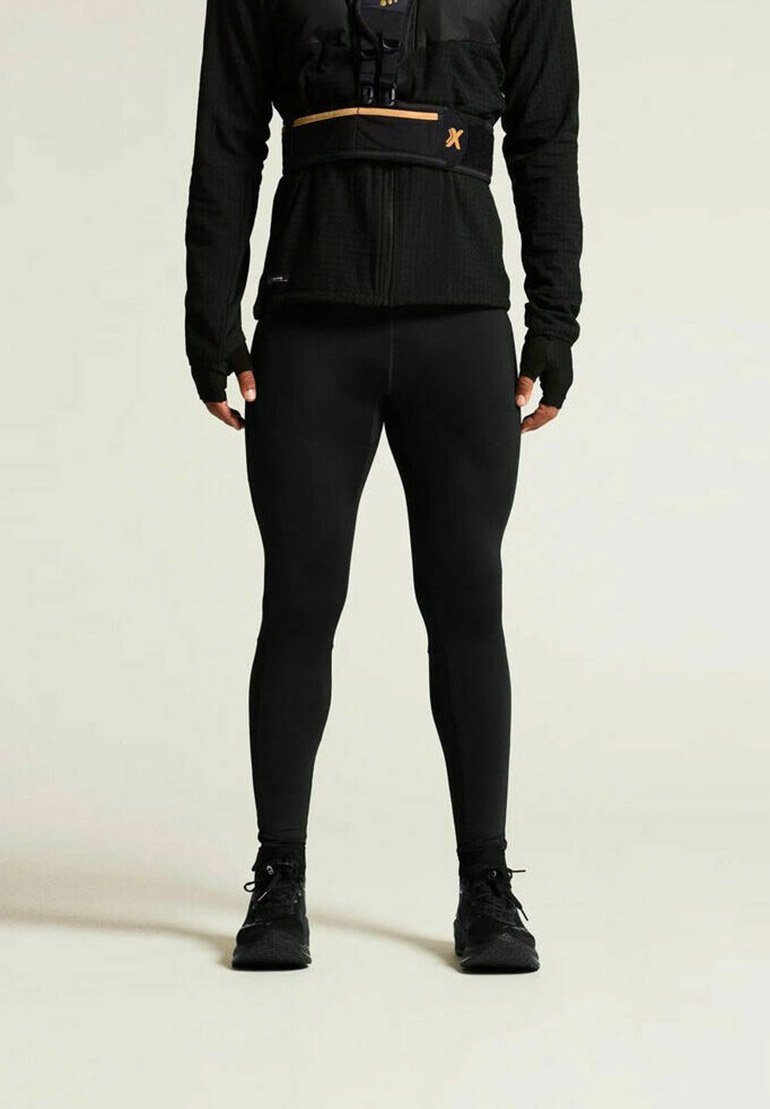 Schwarze Sportleggings kombiniert mit einem strukturierten schwarzen Langarmoberteil mit Reißverschluss und orangefarbenen Akzenten. Zusätzlich schwarze Schuhe.