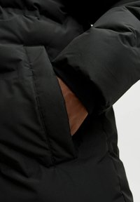 Mustmust must jacket, mille sile ja selgelt nähtava õmblemise detailidega. Pruunist kangast voodriga tasku on osaliselt lahti tõmmatud küljelt.