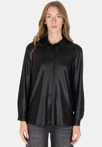 Camicia nera leggera con trama liscia, maniche lunghe, chiusura frontale con bottoni e colletto classico, abbinata a jeans scuri.