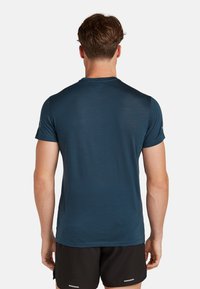 Lyhytnettinen urheilupaita tumman teal-värissä, valmistettu hengittävästä, teksturoidusta kankaasta. Tyylissä on pyöreä kaula-auko ja slim fit -suunnittelu.