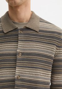Gestreept poloshirt in bruin, beige en blauw. Voorzien van een borstsluiting met knopen en een getextureerde brei met horizontale en opengewerkte patronen.