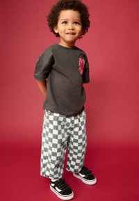 T-shirt gris avec un graphique rose, pantalon baggy gris et blanc à carreaux, et baskets noires avec semelles blanches et attaches Velcro.