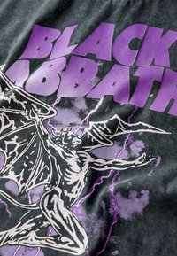 Black Sabbath grafisk t-shirt med en mørkegrå stof og iøjnefaldende lilla bogstaver samt en detaljeret illustration af en vingefigur midt i lyn.