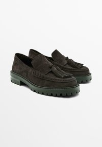 Mocassini in camoscio marrone scuro con finitura testurizzata, suola in gomma verde e nappine decorative sul davanti. Design classico da mocassino.