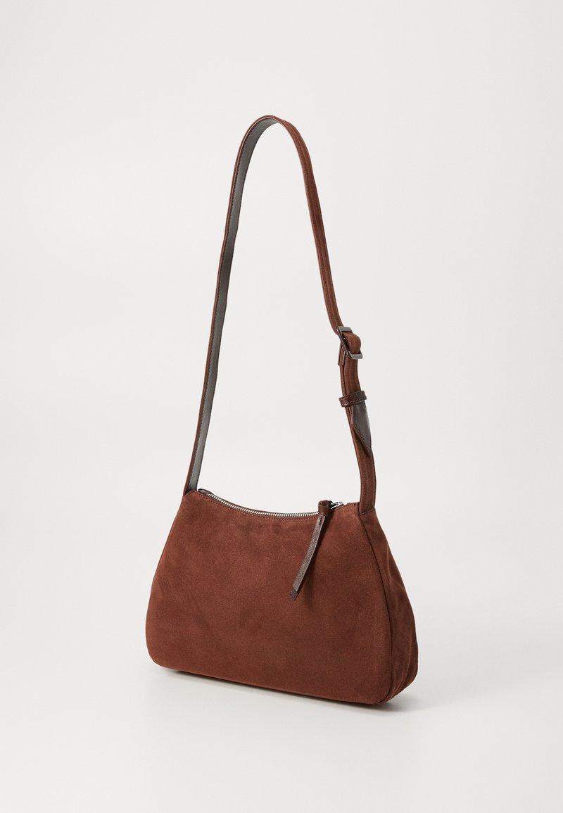 Brown suede handbag with a curved shape and silver zipper, featuring a slim adjustable strap in darker leather. Smooth texture, minimalist design.