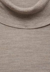 Beige polotröja med ribbat mönster och vikbar krage, i mjukt stickat tyg och sömlös design vid halsringningen.