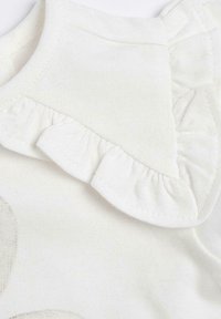 Prenda de algodón blanca con textura suave, que presenta un detalle de escote con volantes y un acabado liso.