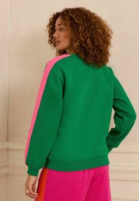 Felpa verde con accenti rosa sulle spalle, maniche lunghe e polsini a costine. Tessuto morbido, vestibilità rilassata, design a girocollo.
