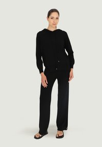 Czarna bluza z kapturem z troczkami i przednią kieszenią, w zestawie z czarnymi spodniami o szerokich nogawkach. Gładka tekstura, luźny krój i minimalistyczny design.