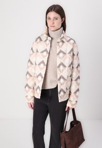 Κουβερτίνα σε παστέλ αποχρώσεις με γεωμετρικό σχέδιο που περιλαμβάνει σχεδίαση ηλιακής έκρηξης. Φτιαγμένη από ύφασμα, με κολάρο και κουμπί.