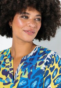 Kleurige blouse met abstracte patronen in blauw, geel en groen. Materiaal lijkt lichtgewicht met een subtiele glans. Opvallend ontwerp van de kraag.