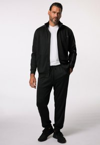 Chándal deportivo negro con chaqueta con cremallera y pantalones con cordón. Presenta ribetes blancos, un escote tipo barco y tejido texturizado.