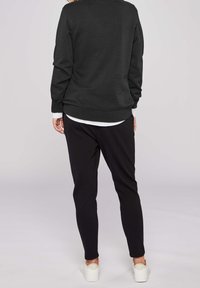 Pull noir à côtes avec manches longues, associé à un pantalon noir fuselé. Comprend une chemise blanche en dessous et des baskets blanches.