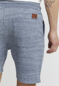 Shorts bleus texturés avec poches latérales et une étiquette de marque en cuir brun à l'arrière. La taille élastique offre confort et flexibilité.