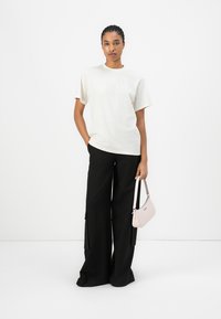 Loose-fitting cream t-shirt with short sleeves, paired with wide black pants and a small pink handbag for contrast.