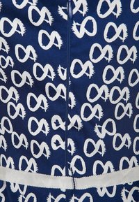 Tessuto blu navy con un motivo a simbolo dell'infinito bianco, chiusura a zip e una fascia bianca orizzontale vicino al bordo inferiore.